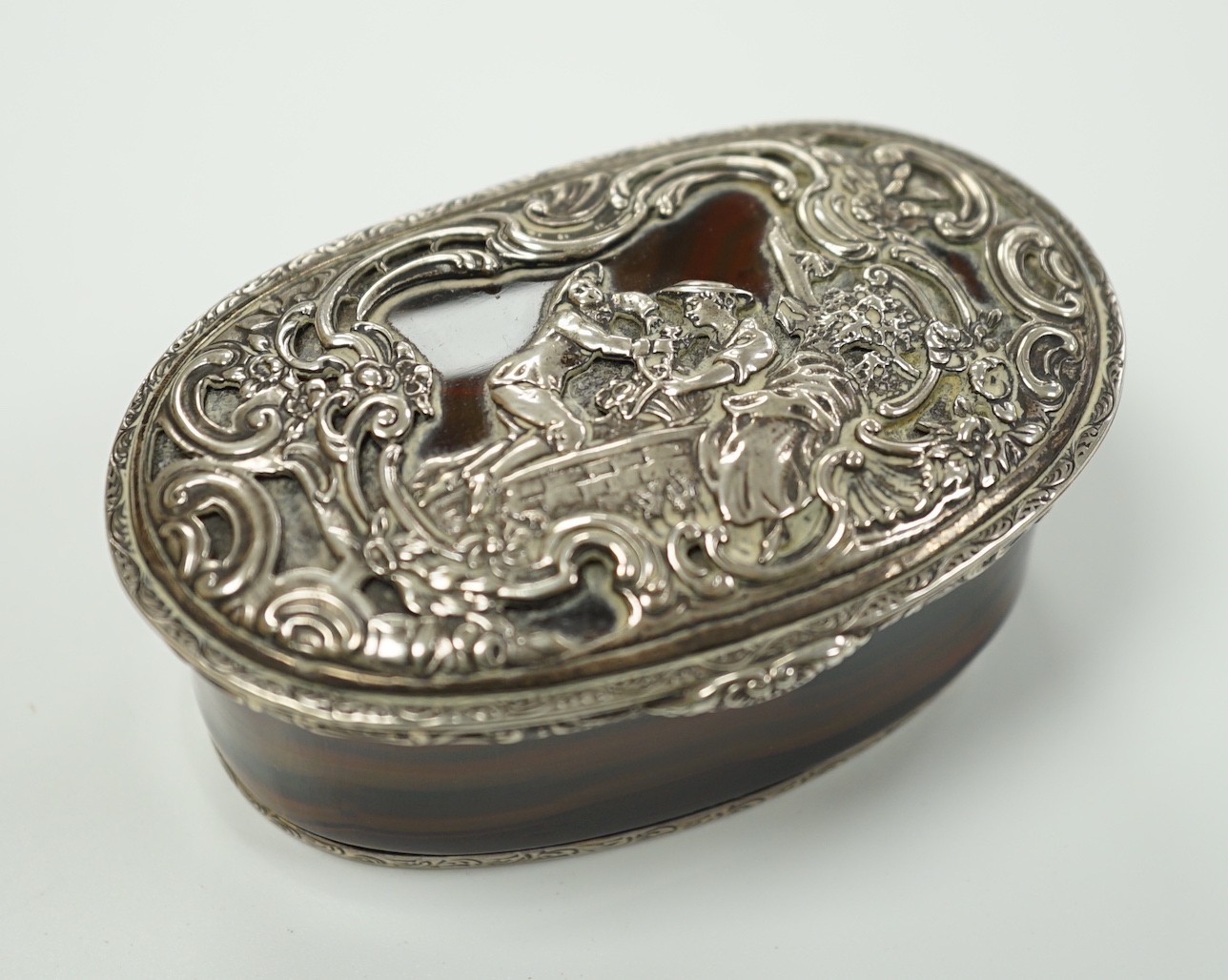 A 19th century continental white metal mounted banded agate oval snuff box, decorated with figures amid scrolls, length 79mm.